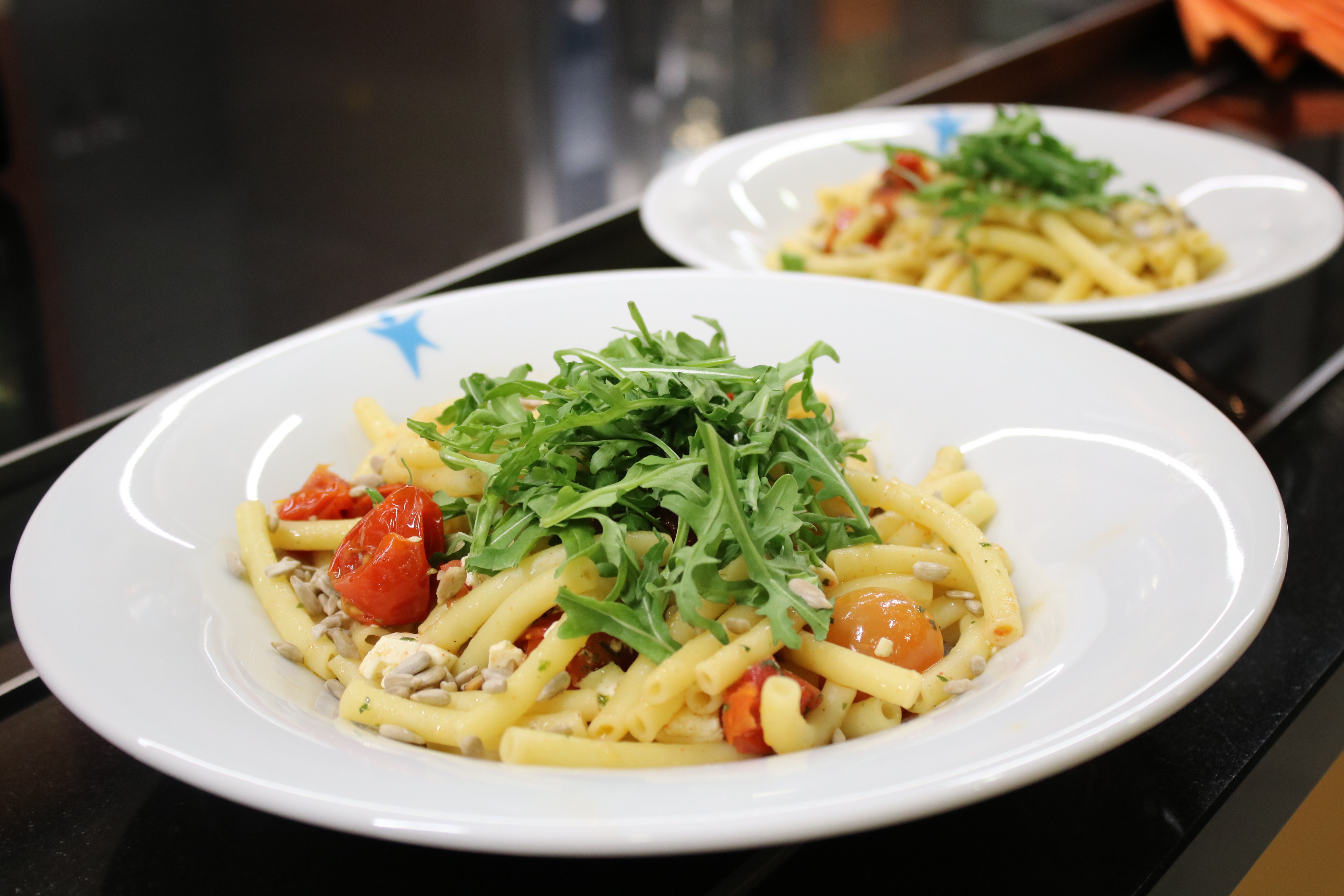 two plates of pasta with tomatoes, pine nuts, and fresh arugula