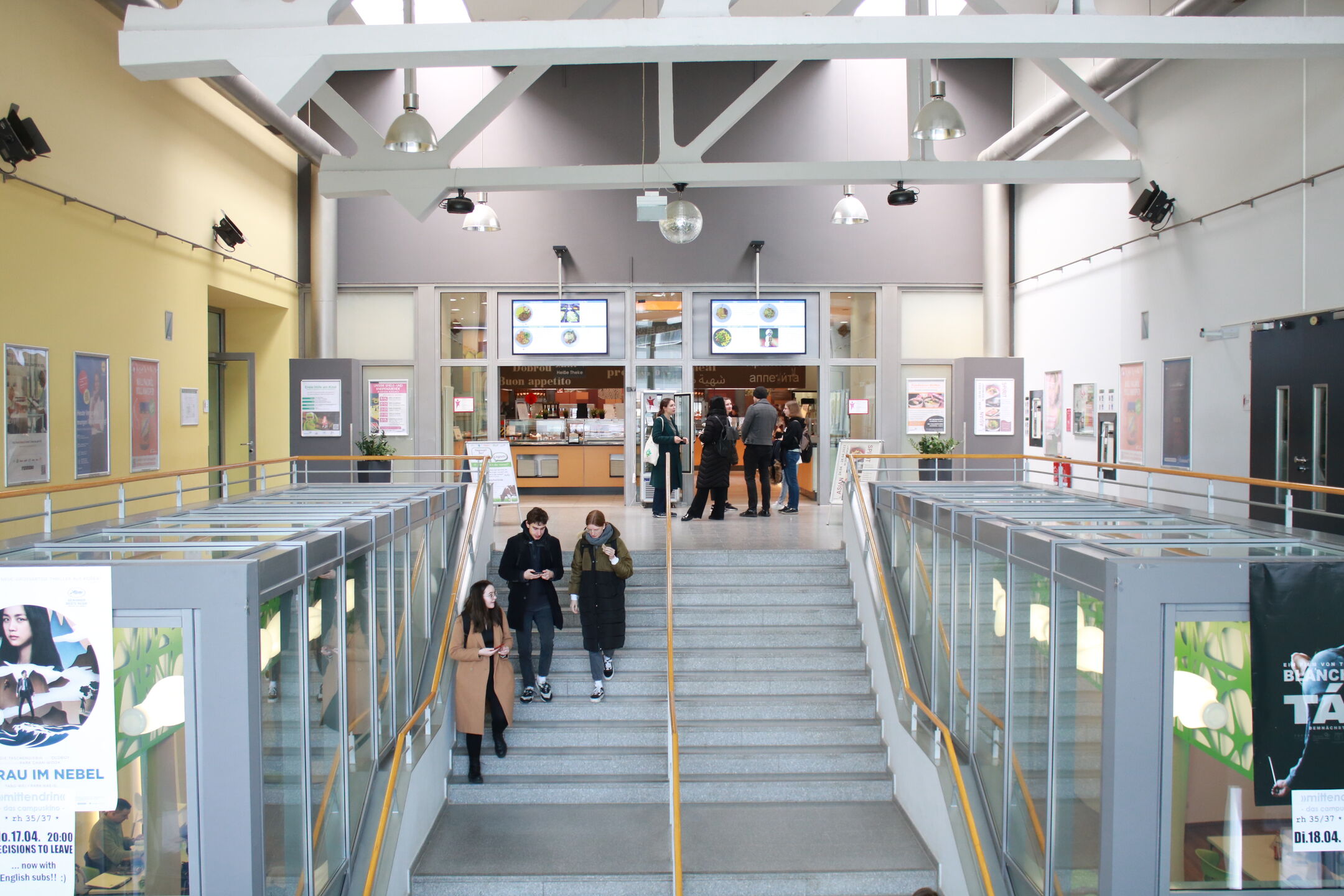 Foyer der Mensa, Treppe mit Studierenden, Plakatrahmen an den Wänden
