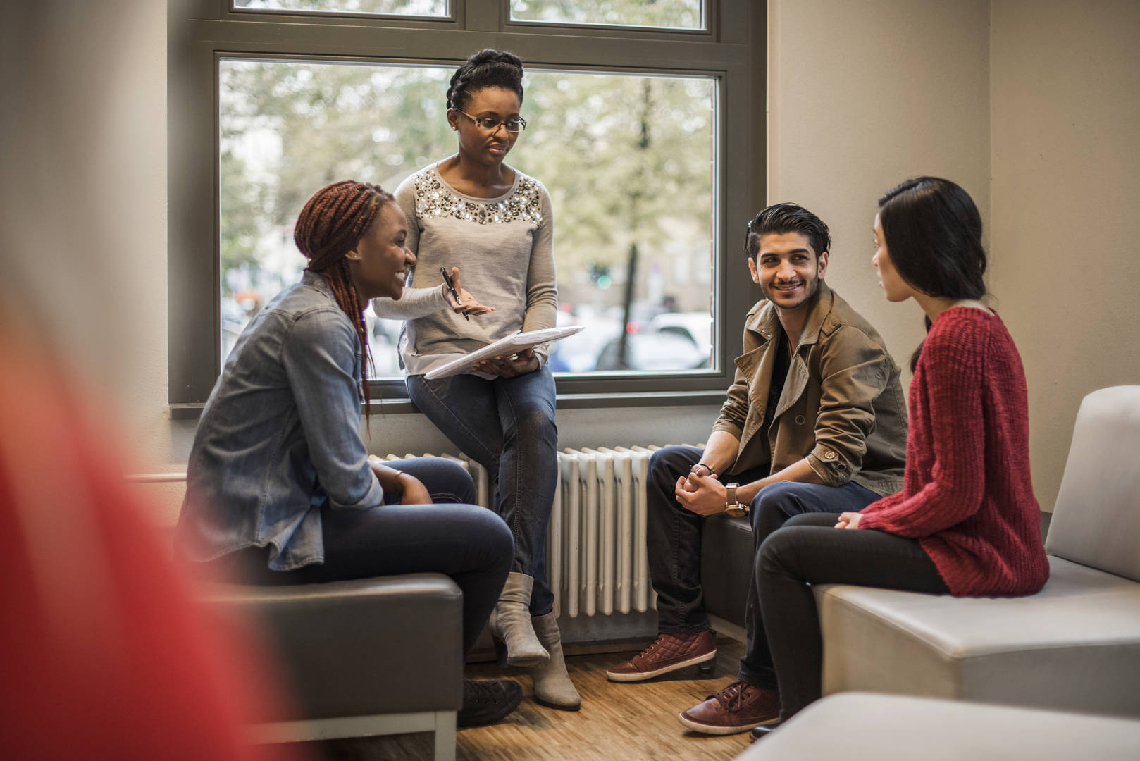 a group of people sitting in a corner; a woman with a notepad and pen is standing next to them