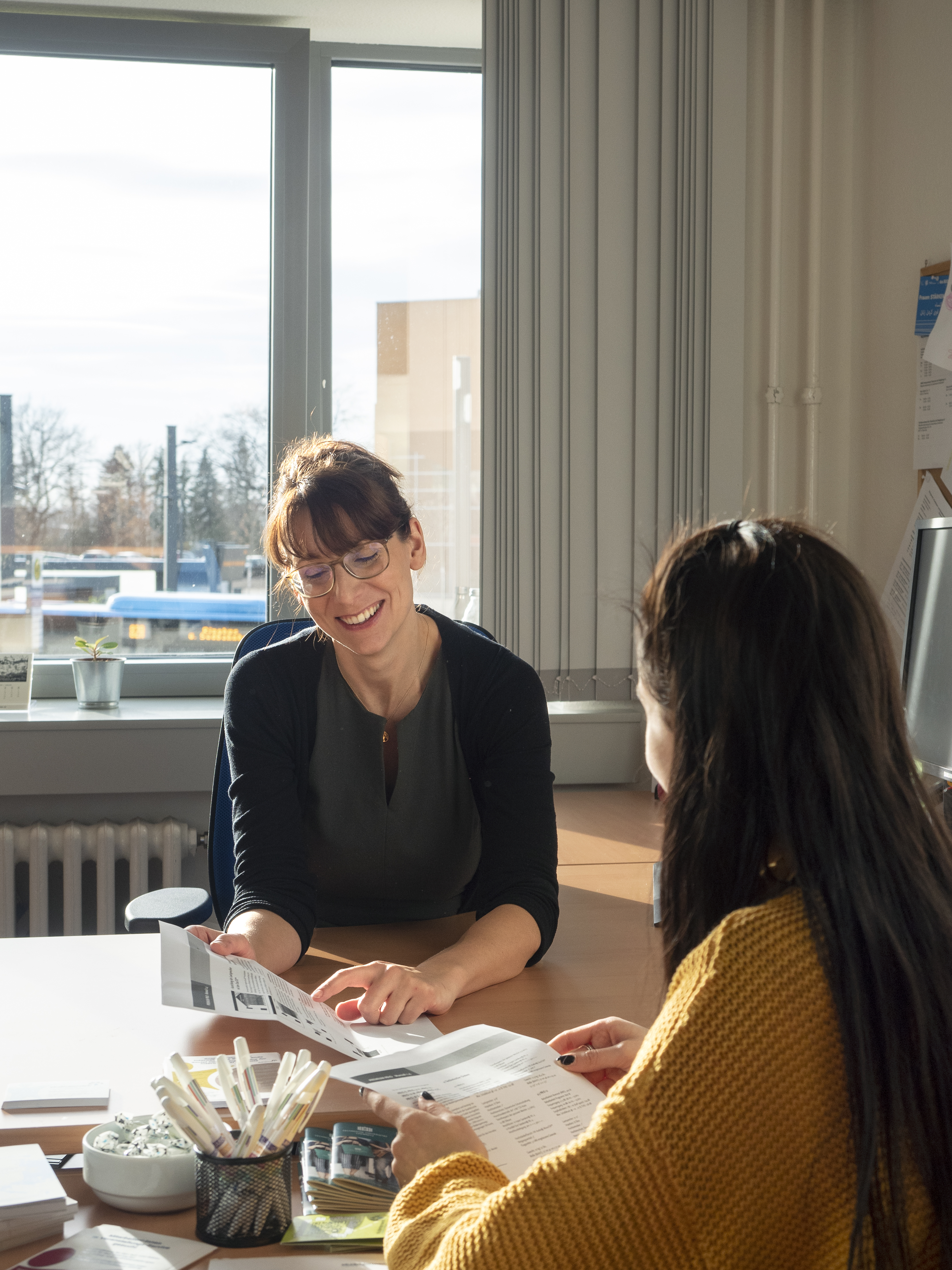 Beratung an einem Tisch, lächelnde Frau zeigt etwas auf einem Blattpapier